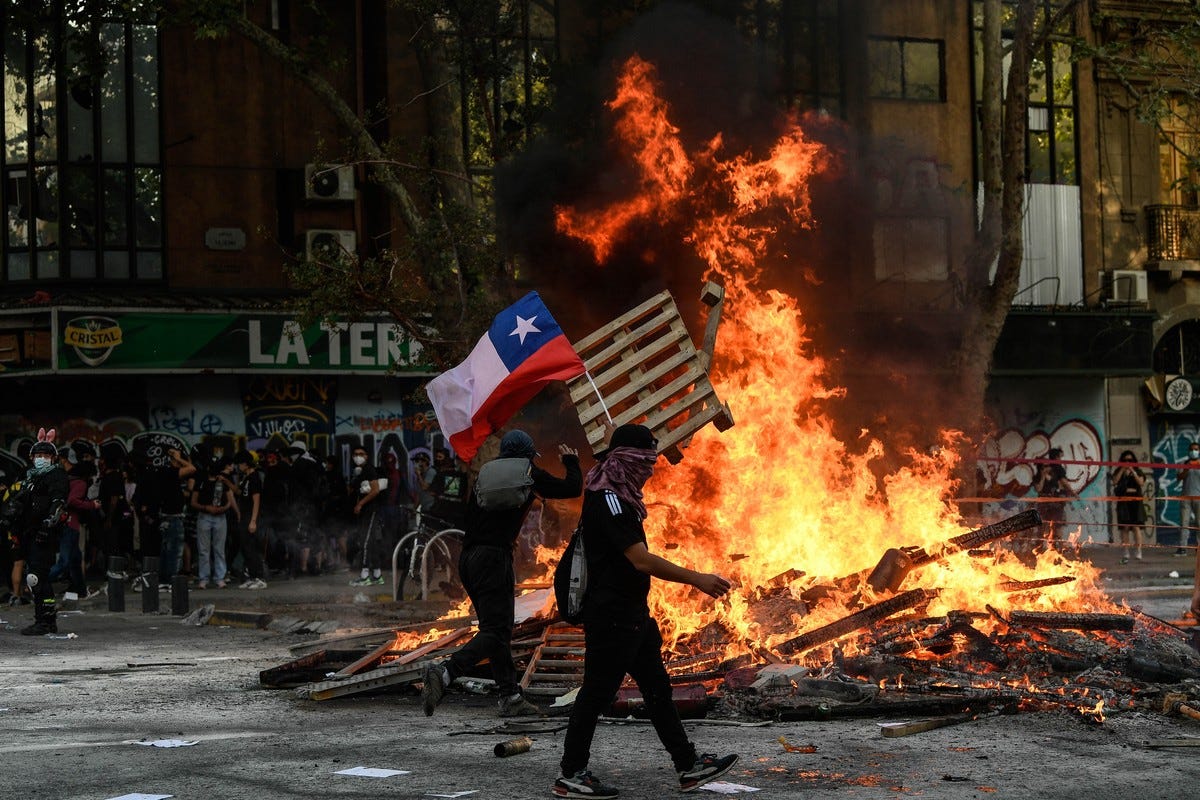 Chile 2019 protests with demonstrators and Chilean flag in front of burning barricade — example of opportunity cost driving life decisions, Beating the Tide investing newsletter.