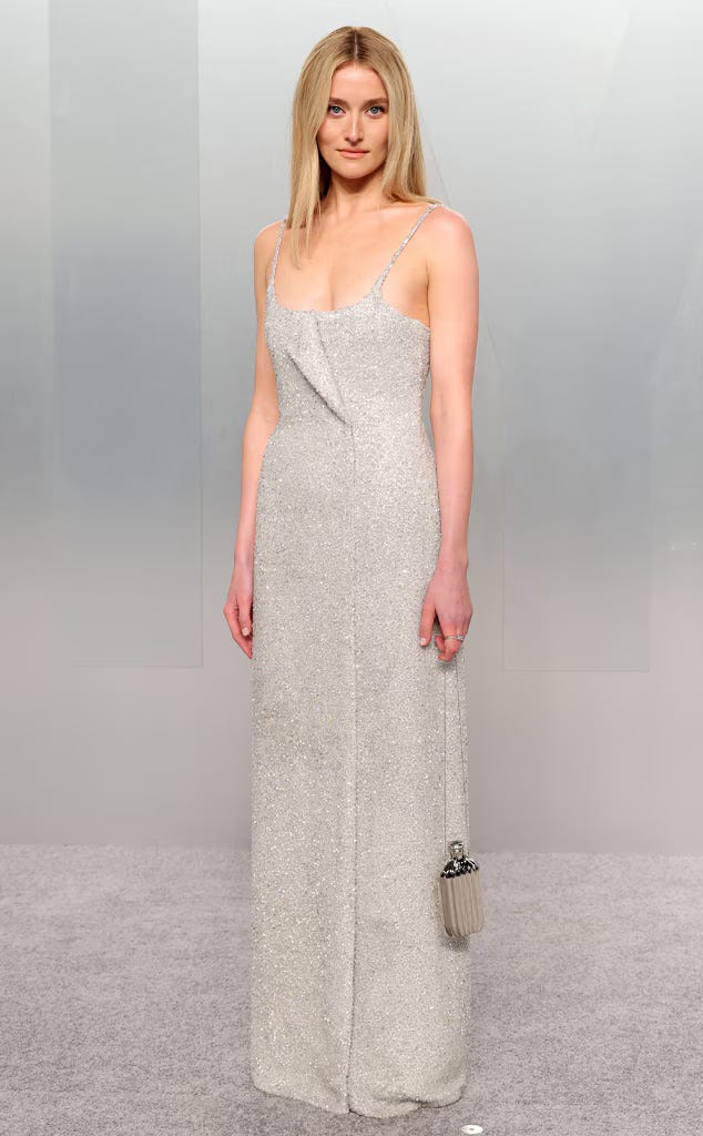 Sarah Pidgeon on the Oscars red carpet wearing a shimmering silver sequined Calvin Klein Collection gown with delicate spaghetti straps and a deconstructed neckline, carrying a clutch shaped like a CK One perfume bottle. Sarah Pidgeon on the Oscars red carpet wearing a shimmering silver sequined Calvin Klein Collection gown with delicate spaghetti straps and a deconstructed neckline, carrying a clutch shaped like a CK One perfume bottle.