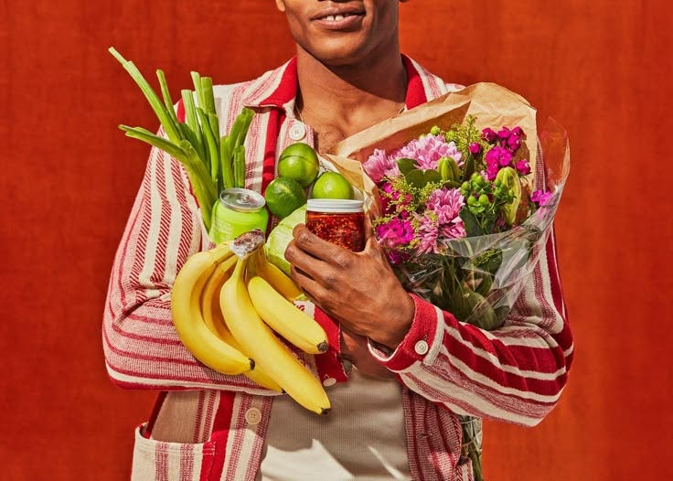This may contain: a man holding a bunch of fruit and flowers in his hands while standing against a red wall This may contain: a man holding a bunch of fruit and flowers in his hands while standing against a red wall