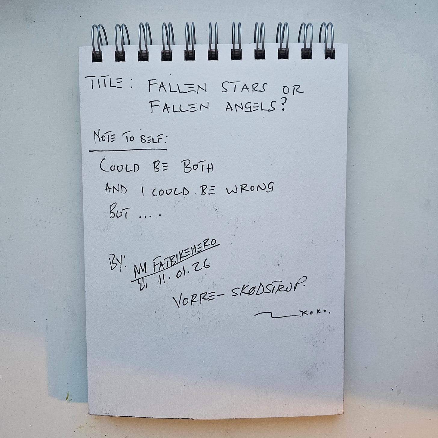 Alt Text:  The back of a sketchbook page showing handwritten notes in black ink. Text reads: "TITLE: FALLEN STARS OR FALLEN ANGELS? NOTE TO SELF: COULD BE BOTH AND I COULD BE WRONG BUT.... BY: M FATBIKEHERO 11.01.26 VORRE-SKØDSTRUP. xoxo."