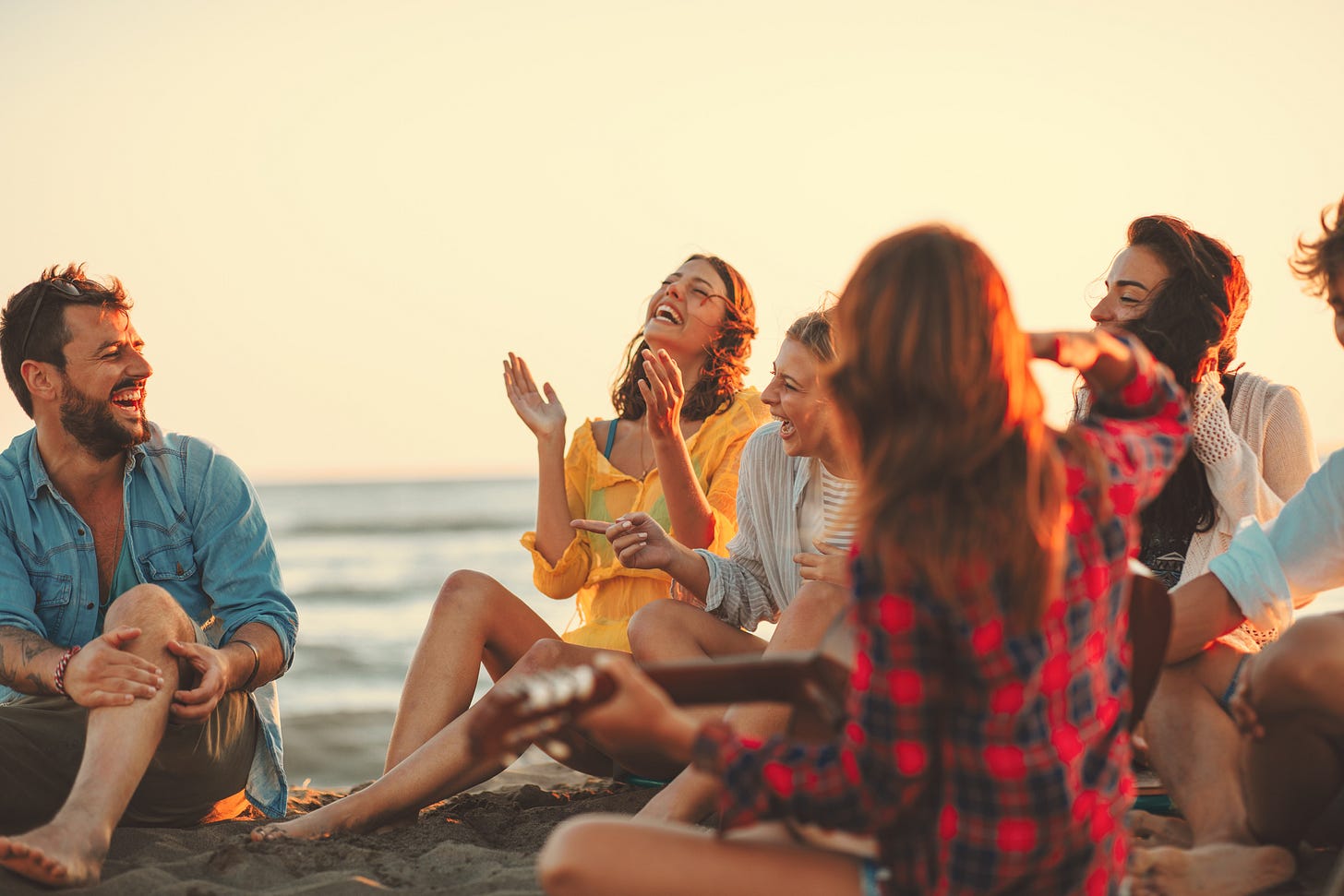 A group of friends sitting around the beach at dusk, laughing