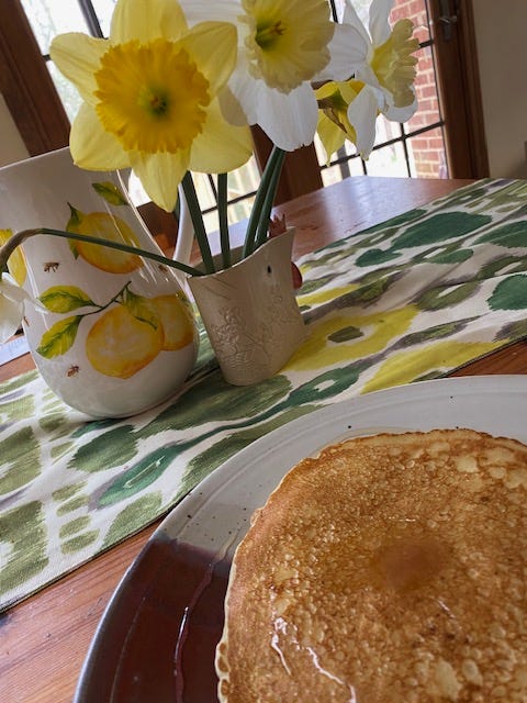 pancakes on a table next to daffodils and a pitcher covered in lemons