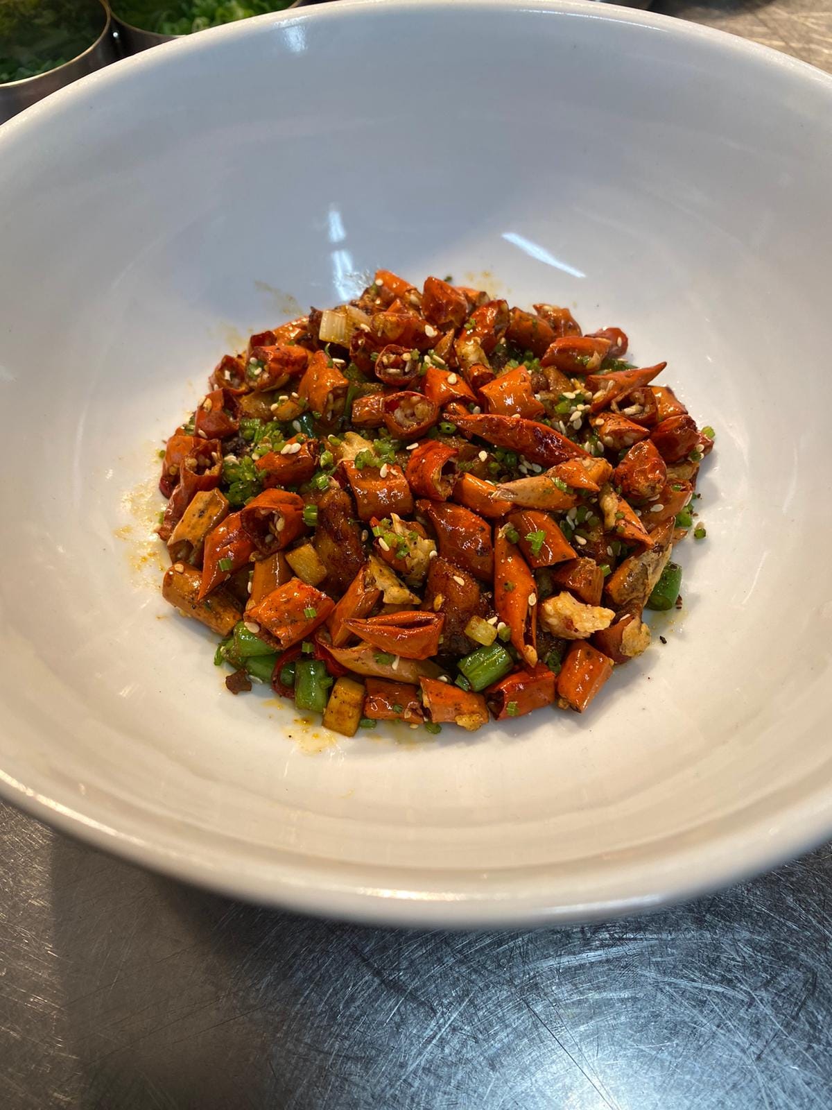 an overhead shot of a white dish on a stainless steel surface. In the dish is a pile of cooked red chillies, herbs, vegetables and chicken. an overhead shot of a white dish on a stainless steel surface. In the dish is a pile of cooked red chillies, herbs, vegetables and chicken.
