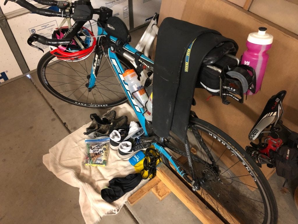Triathlon transition set-up with a blue Fuji triathlon bike, and various equipment for the swim, bike, and run legs of a race laid carefully on a towel under the bike, the wetsuit hanging over the bike, and the helmet hanging from the aerobars. Triathlon transition set-up with a blue Fuji triathlon bike, and various equipment for the swim, bike, and run legs of a race laid carefully on a towel under the bike, the wetsuit hanging over the bike, and the helmet hanging from the aerobars.