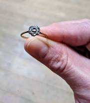 A hand holding a small diamond cluster ring with the central stone missing. A hand holding a small diamond cluster ring with the central stone missing.