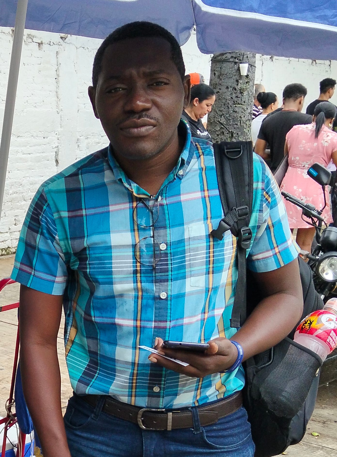 A man in a blue plaid shirt stands under a blue umbrella