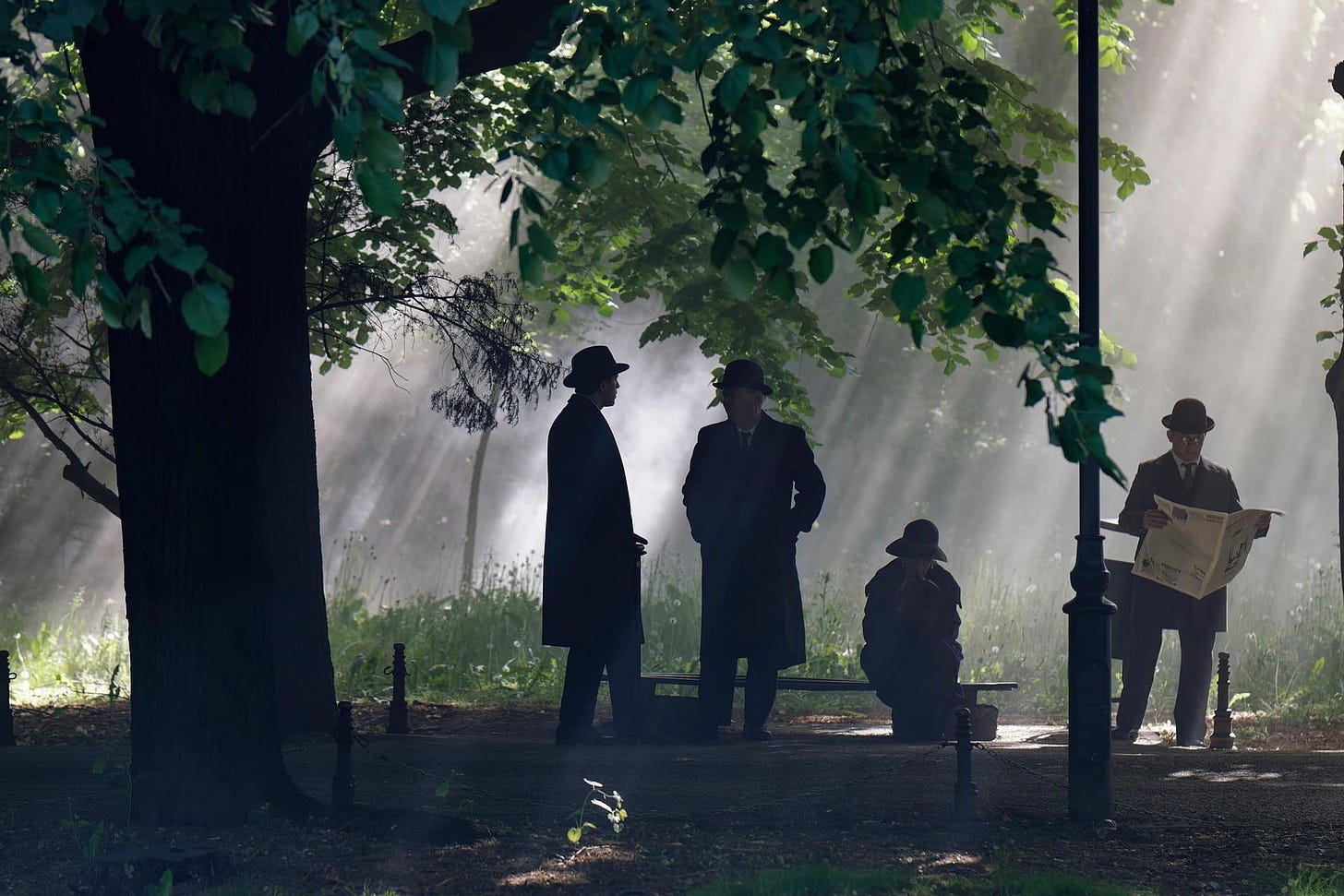 Two men converse in a park while a third reads a newspaper.