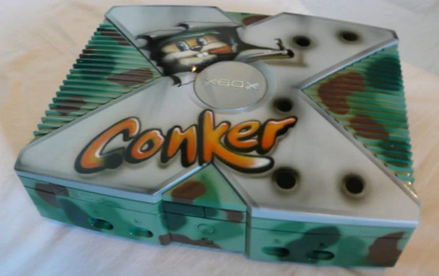 Custom Xbox console with "Conker" graffiti and a cartoon character. Camouflage pattern, set on a light surface. Vibrant and playful mood.