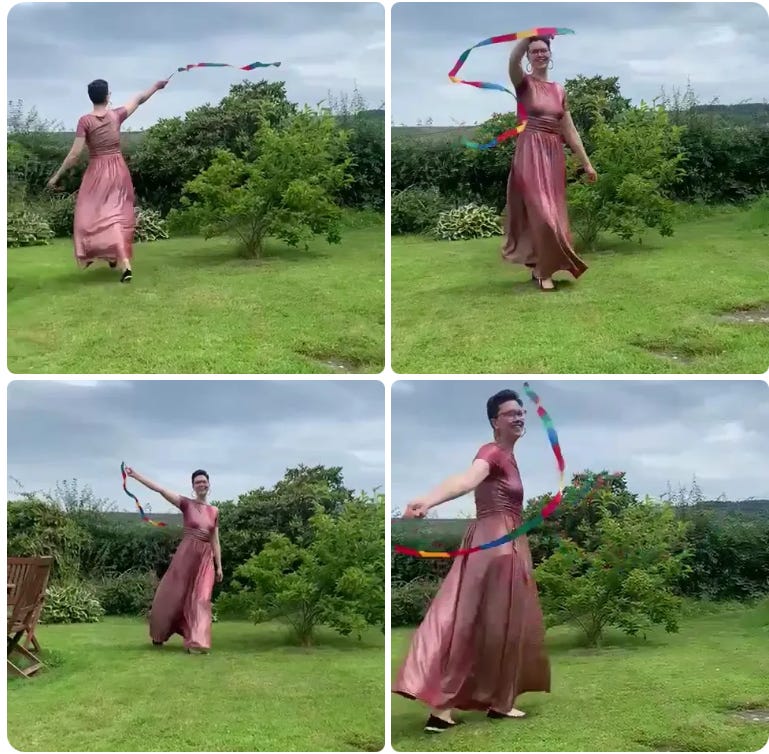 Janelle (white woman with very short brown hair) in a long pink dress smiling and dancing around waving a multi-coloured ribbon outside on green grass Janelle (white woman with very short brown hair) in a long pink dress smiling and dancing around waving a multi-coloured ribbon outside on green grass