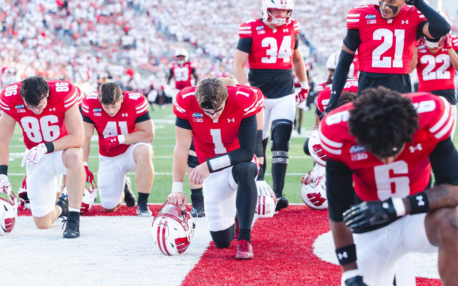 Wisconsin Badgers football players kneel together in the end zone for a prayer before a game. Wisconsin Badgers football players kneel together in the end zone for a prayer before a game.