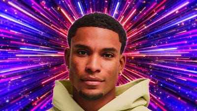 A head and shoulders shot of a man in a bright hoodie, smiling to camera, set against a sparkling purple, pink and blue background A head and shoulders shot of a man in a bright hoodie, smiling to camera, set against a sparkling purple, pink and blue background