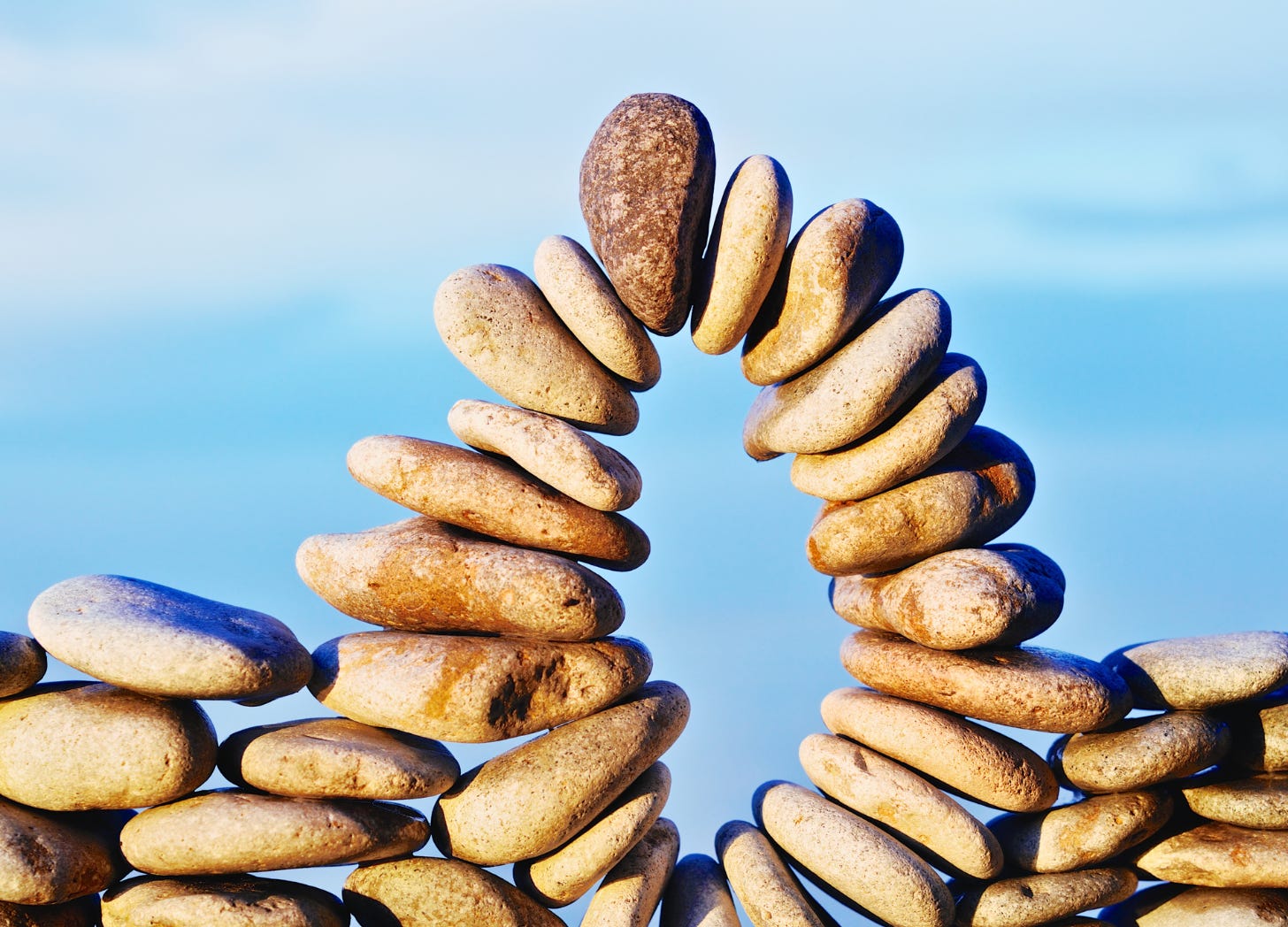 Stacked stones arranged in an open arch, showing balance created through responsiveness rather than uniform strength.