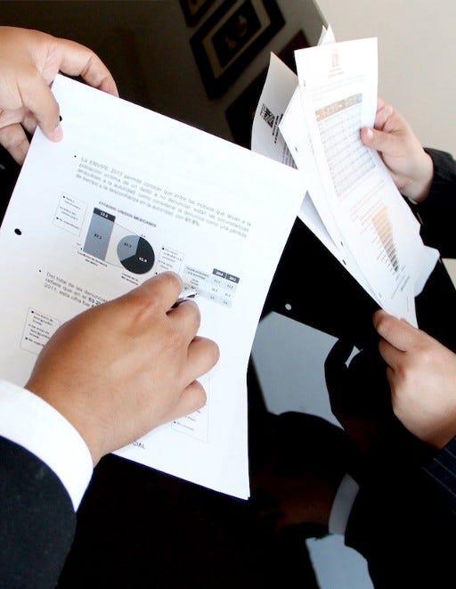 Two sets of hands going over a report. One is pointing at a graph and wearing a business suit, while the other set of hands is reading over the rest of the report. Two sets of hands going over a report. One is pointing at a graph and wearing a business suit, while the other set of hands is reading over the rest of the report.