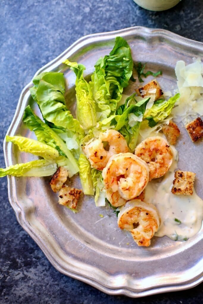 a shrimp and greens salad on silver plate on a blue table. a shrimp and greens salad on silver plate on a blue table.