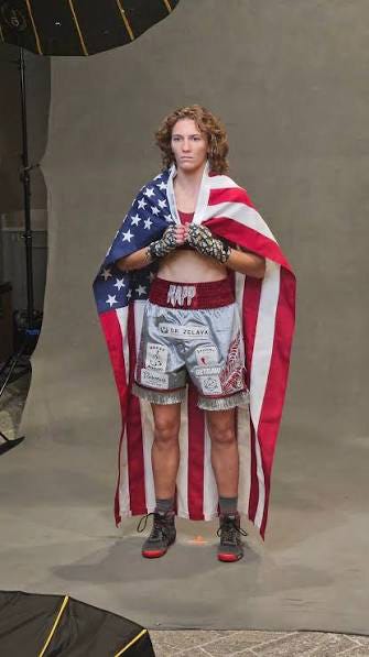 Boxer Hannah Rapp draped in an American flag, wearing silver boxing shorts with a red waistband and red boxing shoes. Boxer Hannah Rapp draped in an American flag, wearing silver boxing shorts with a red waistband and red boxing shoes.