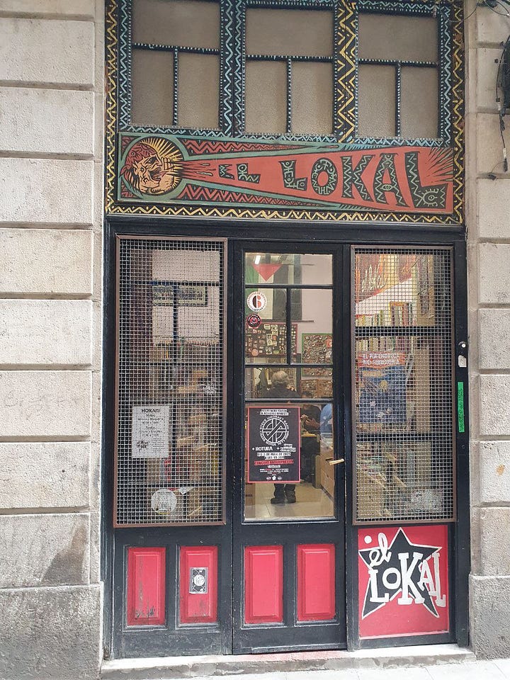 Storefront of the Bookshop in red and black, and a foto of a Black woman and a white man holding a poster between them, surrounded by books. 