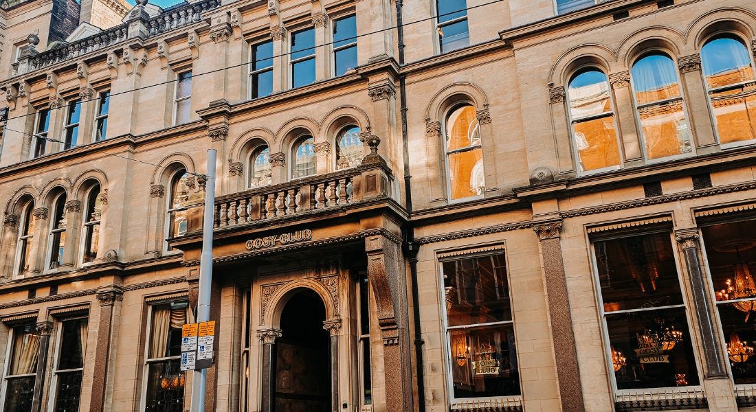 Nottingham's Cosy Club - a large light brown building with rectangular and arched windows, with glowy lights inside