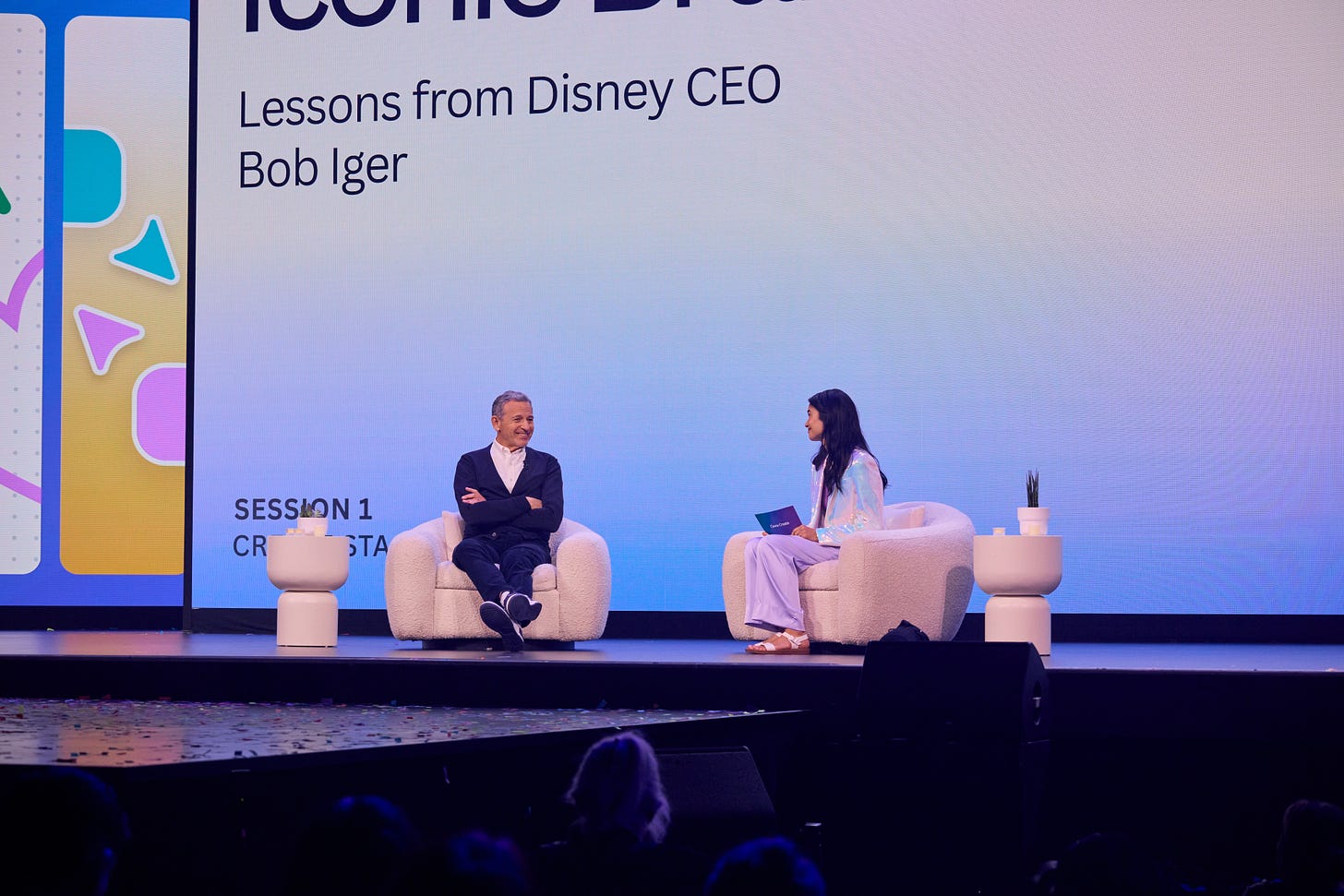 Canva CEO Mel Perkins and Disney CEO Bob Iger on stage in facing chairs at Canva Create 2024. The text on screen behind them reads Lessons from Disney CEO Bob Iger