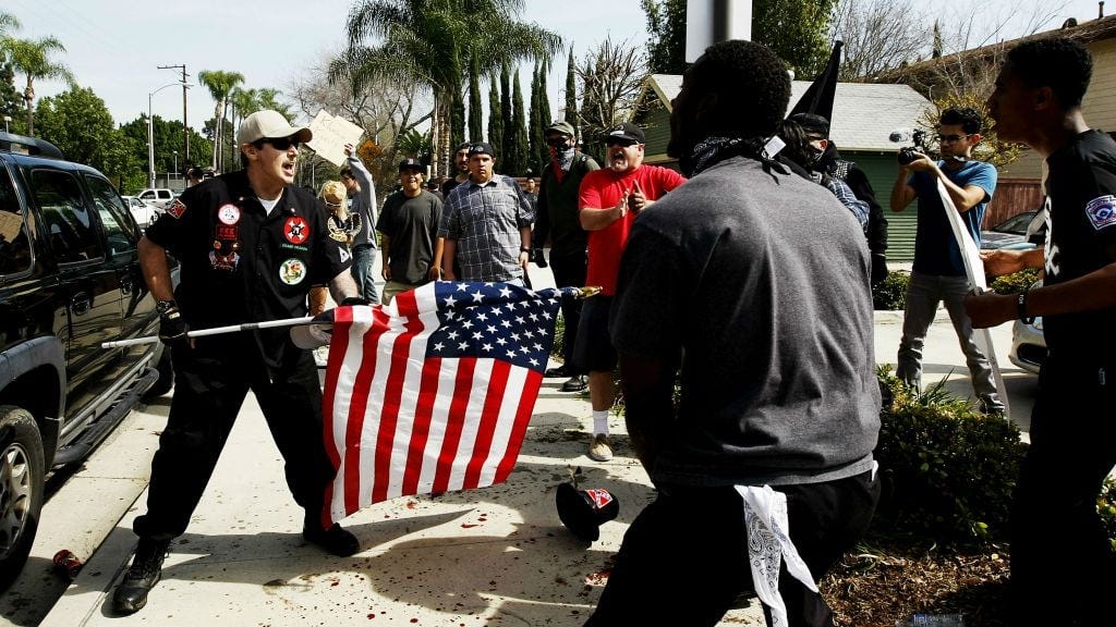 A Ku Klux Klansman, left, uses an American flag to fend off angry counter protesters after members of the KKK tried to start a 'White Lives Matter' rally at Pearson Park in Anaheim, California, on Saturday, Feb. 27, 2016