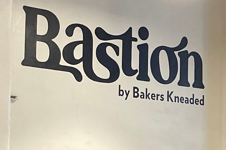 a gooey chocolate chip cookie and the wall mural of the bakery's name