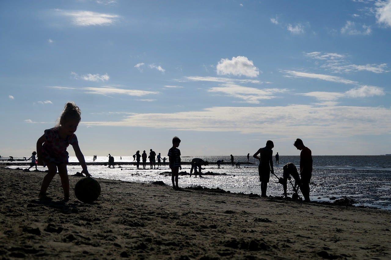 a photo of children and others scattered along the beach/ocean. they appear mostly as silhouettes, without distinguishing characteristics. a photo of children and others scattered along the beach/ocean. they appear mostly as silhouettes, without distinguishing characteristics.
