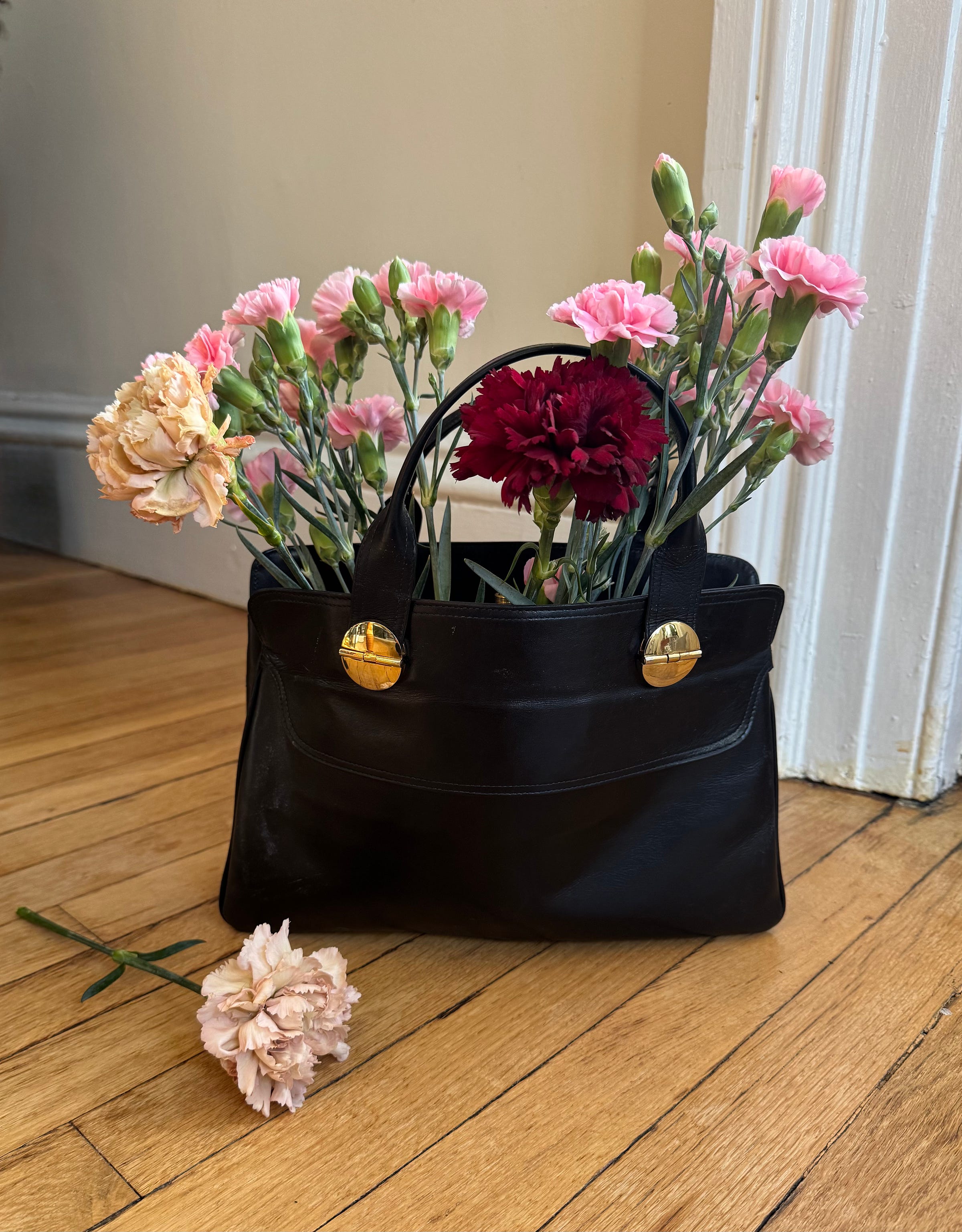 A vintage black leather handbag filled with fresh flowers on a wooden floor in Brooklyn Heights. A vintage black leather handbag filled with fresh flowers on a wooden floor in Brooklyn Heights.