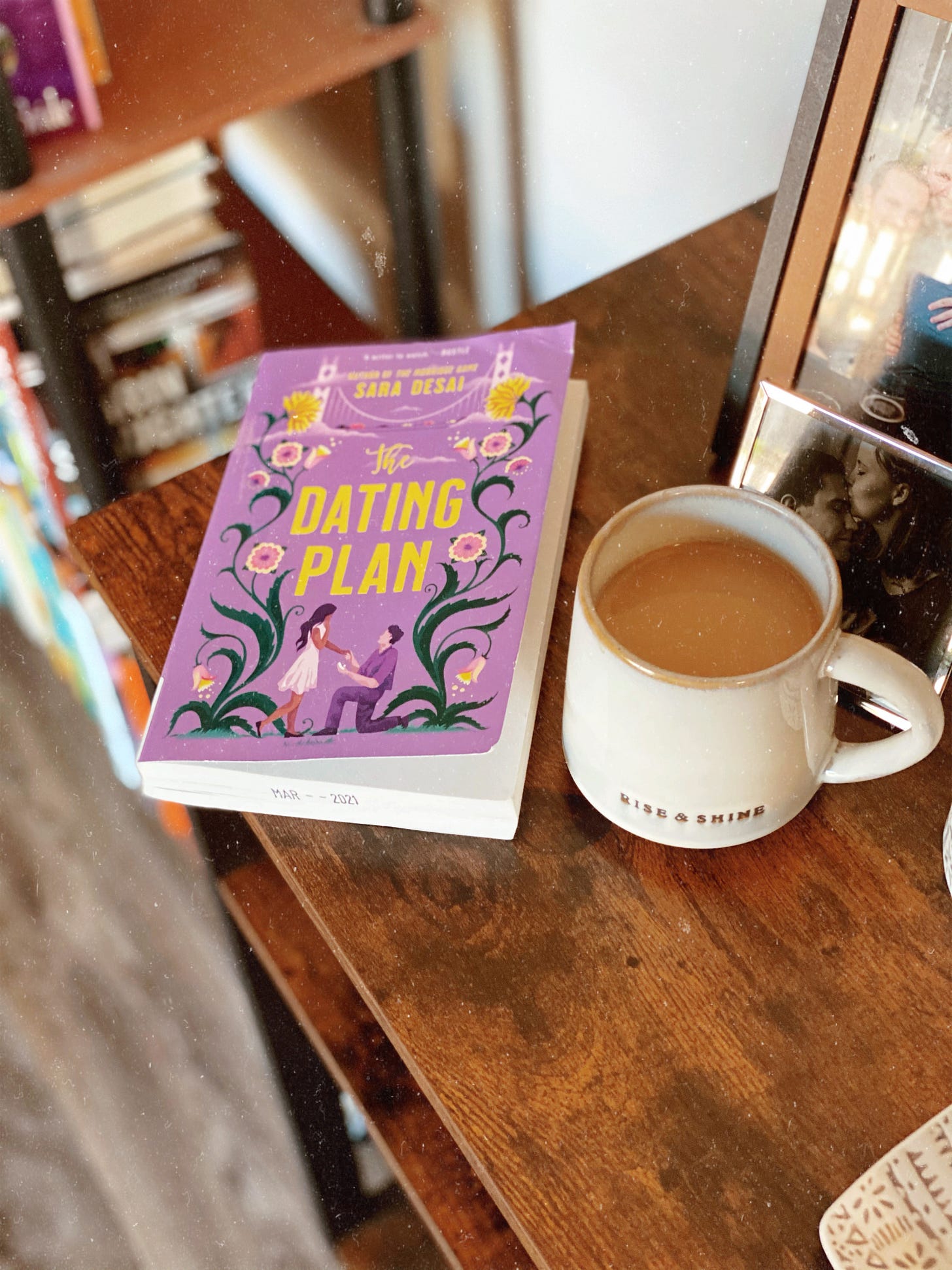 A photo of The Dating Plan sitting on a dark wood coffee table. A cup of coffee is set down to the right of the book. The book cover is a light purple, with yellow lettering.