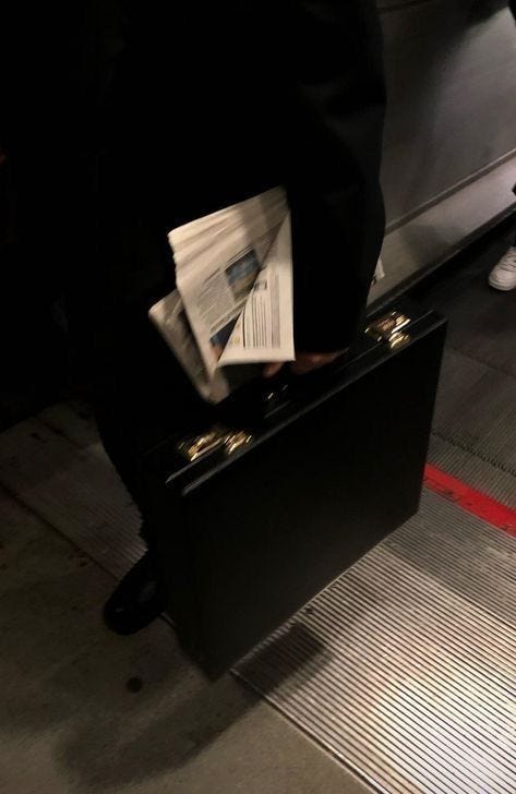 This may contain: a man in suit and tie carrying a black briefcase with papers on the handle,