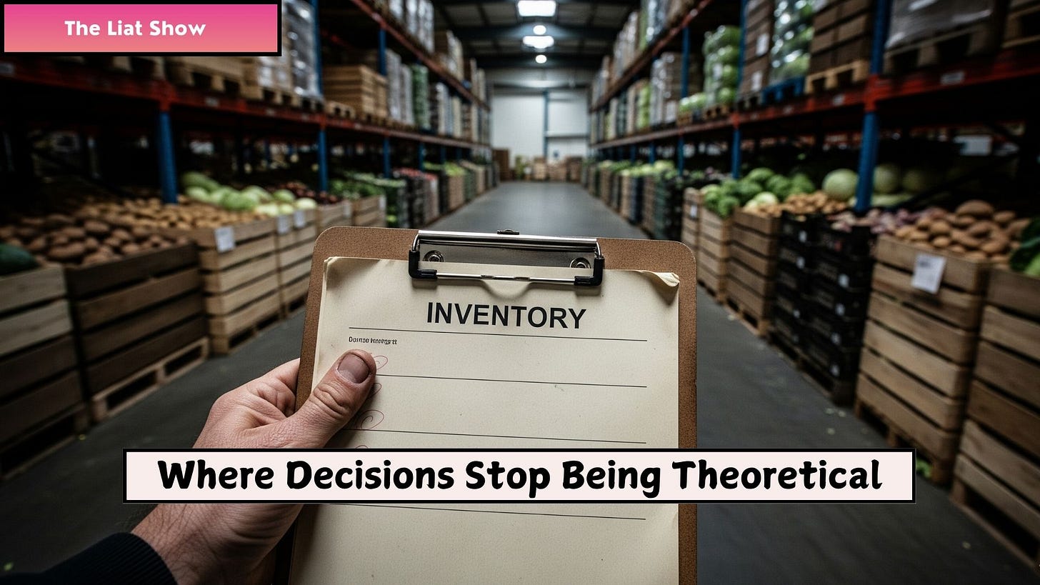 Liat Portal for The Liat Show: Inventory clipboard inside a produce warehouse. Liat Portal for The Liat Show: A hand holds a clipboard labeled INVENTORY in the center of a warehouse aisle filled with stacked produce crates, showing how inventory decisions exist as physical items in storage, not abstract numbers, and how accountability begins at the item level inside real food operations.
