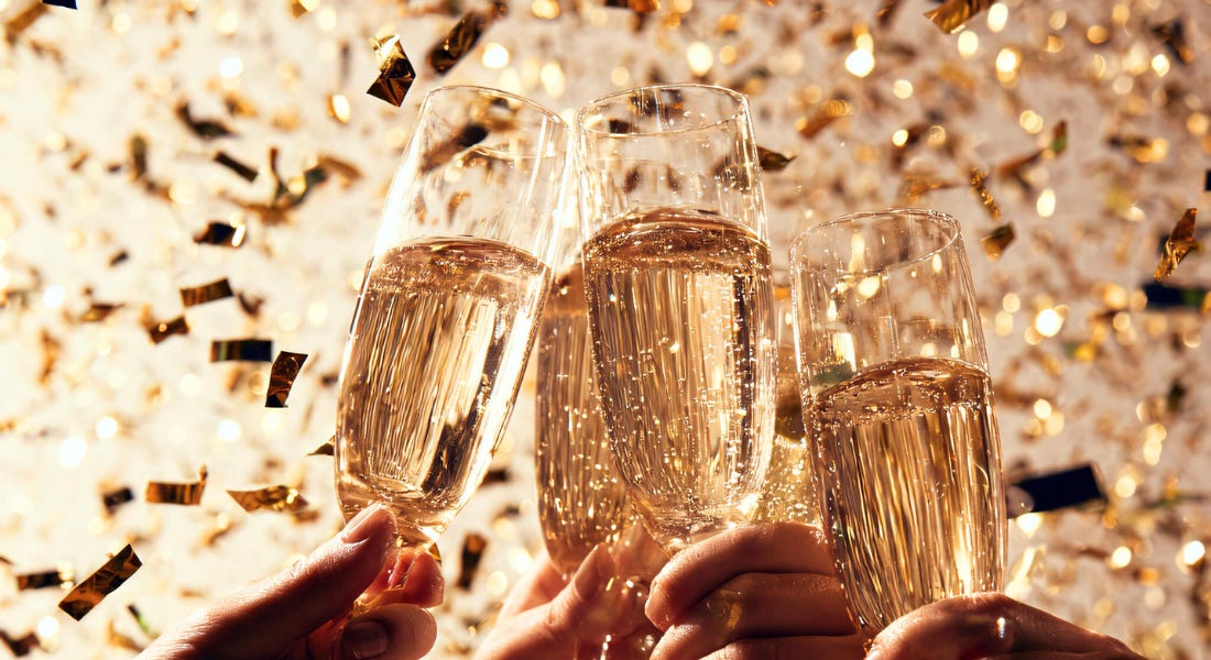 Four champagne glasses being clinked together, with gold confetti around them