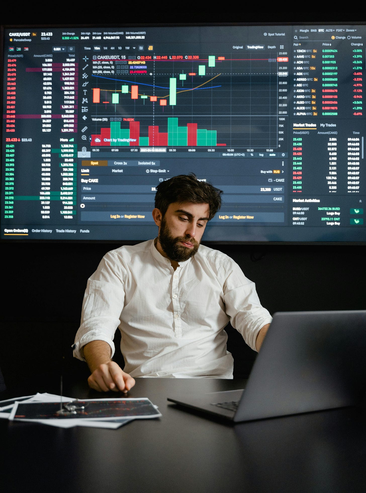 Founder analyzing financial data and stock charts on a large trading screen with laptop in front.
