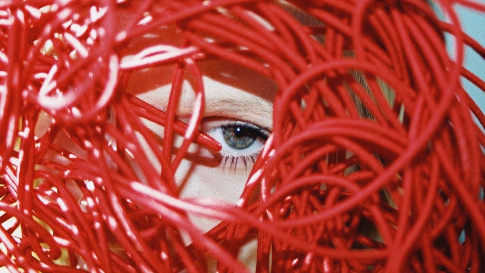 An eye peering through a tangle of red wires