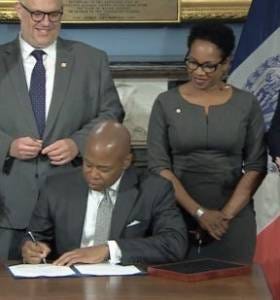 NYC Councilmember Kamillah Hanks looks on while political ally Mayor Eric Adams signs legislation.