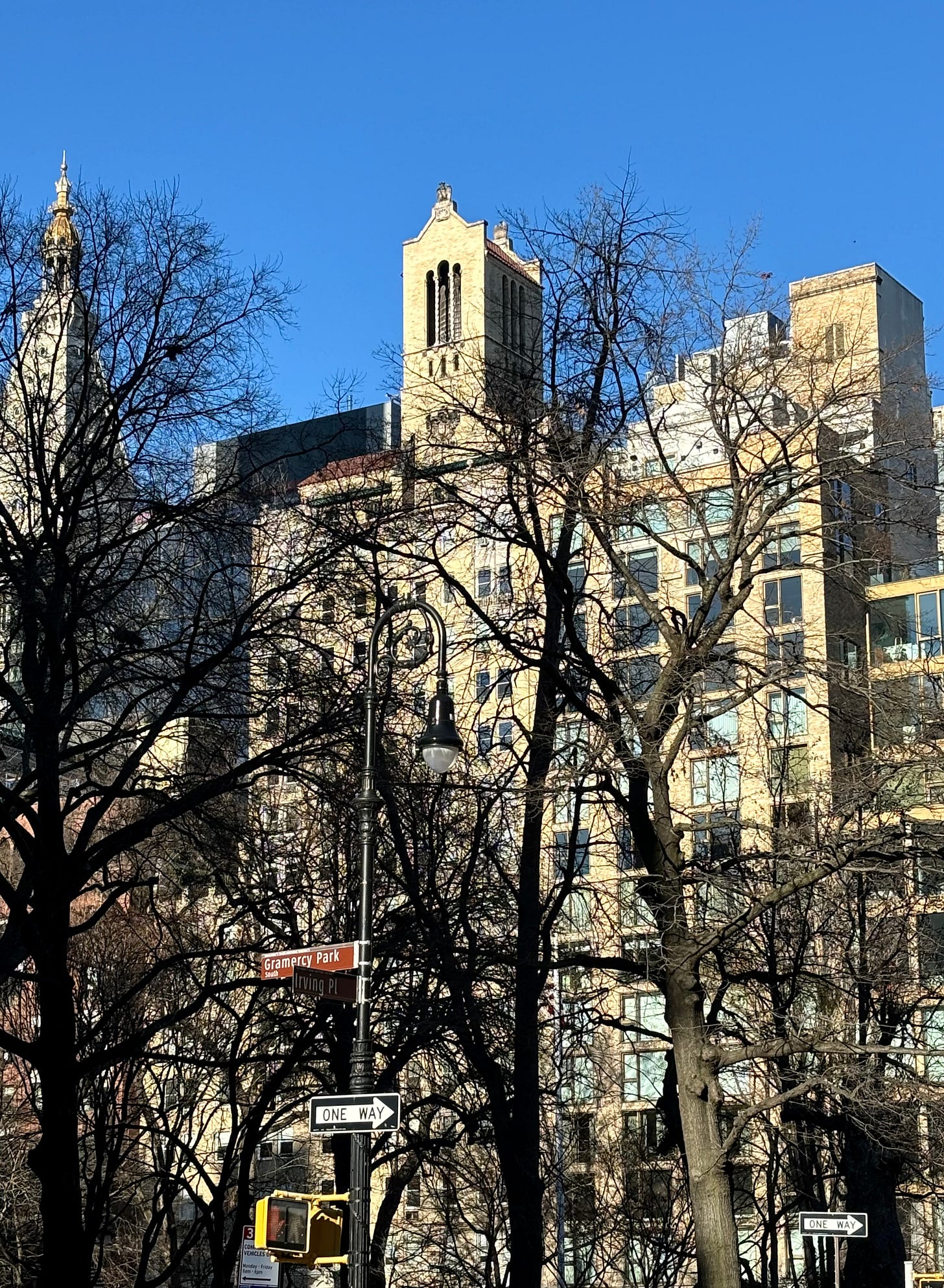 Bare winter trees in front of a luxury coop designed with Spanish and Italian motifs. There is a water tower just visible in a very ornate tower with twisted columns.