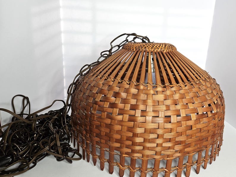 May include: A woven brown pendant light fixture with a rounded shade and a chain for hanging. The shade is made of woven bamboo strips and has a textured appearance. The light fixture is designed for indoor use. May include: A woven brown pendant light fixture with a rounded shade and a chain for hanging. The shade is made of woven bamboo strips and has a textured appearance. The light fixture is designed for indoor use.