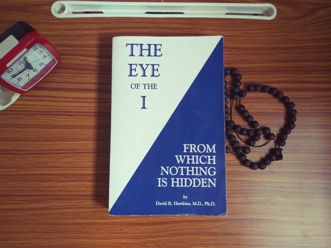 Photo of The Eye Of The I lying on a brown desk alongside a rosery-beaded chain