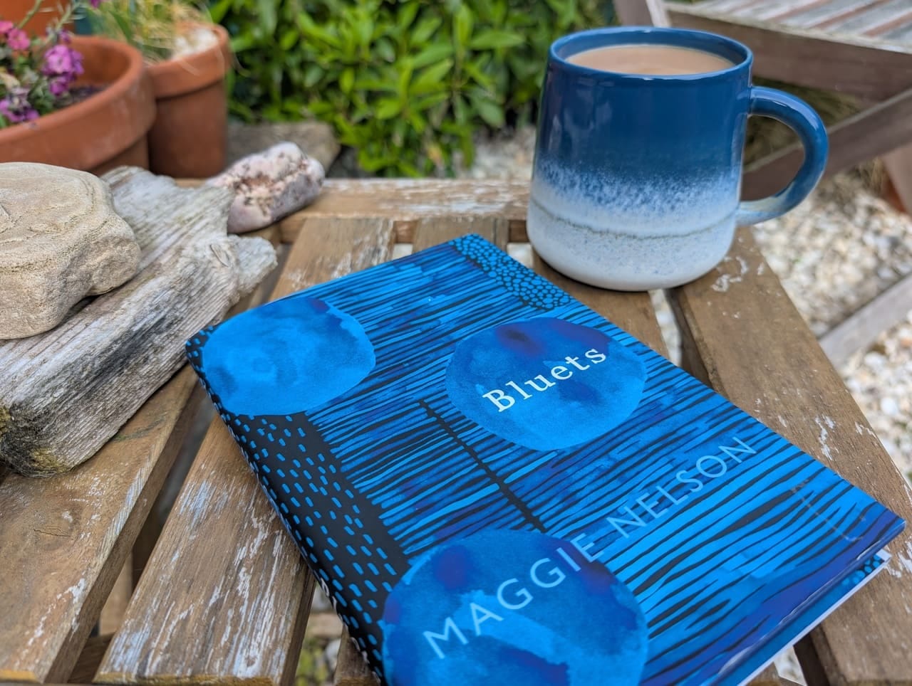 Bluets by Maggie Nelson, on a garden table with coffee in a blue and white mug