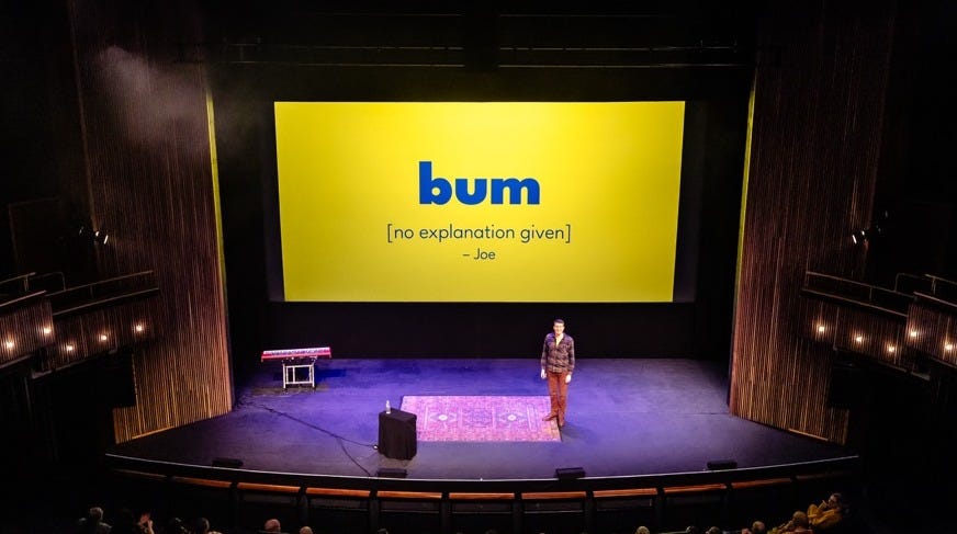 Photo of Rob on stage with the word "bum" on the screen behind him.