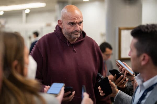 Senator John Fetterman listening to reporters while wearing a burgundy hoodie. 