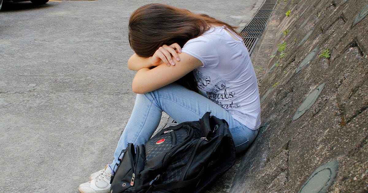 Imagem de uma jovem sentada com a cabeça entre as mãos, denotando profundo sofrimento Imagem de uma jovem sentada com a cabeça entre as mãos, denotando profundo sofrimento