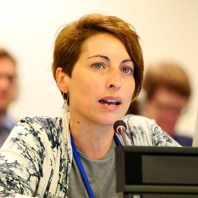 Profile photo of blonde short-haired woman speaking at a conference mic