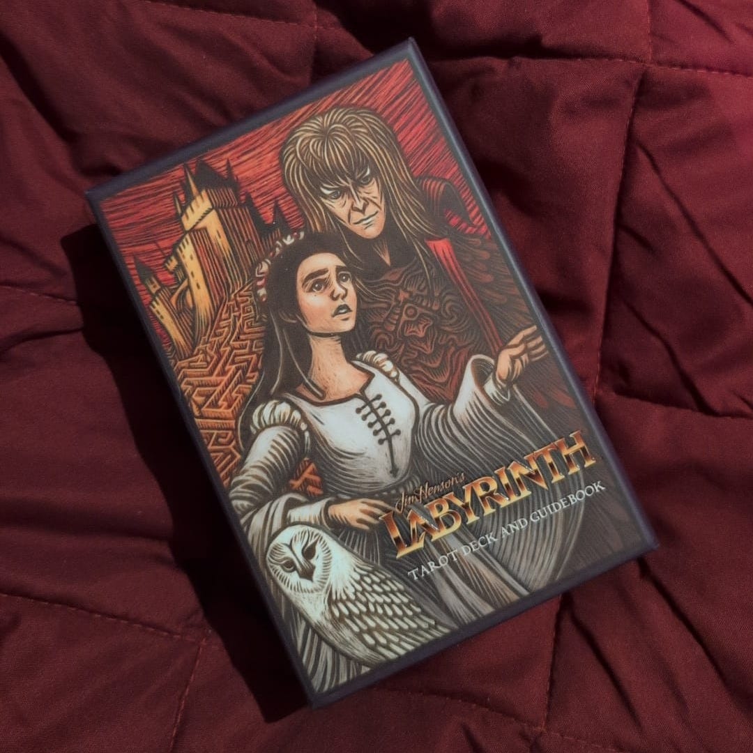 Jim Henson’s Labyrinth Tarot Deck and Guidebook resting on a burgundy quilted blanket, showing Sarah, Jareth and an owl on the illustrated box. Photo shared by Amy Twigg during her Tarot DMs interview about tarot decks, Labyrinth and writing inspiration. Jim Henson’s Labyrinth Tarot Deck and Guidebook resting on a burgundy quilted blanket, showing Sarah, Jareth and an owl on the illustrated box. Photo shared by Amy Twigg during her Tarot DMs interview about tarot decks, Labyrinth and writing inspiration.
