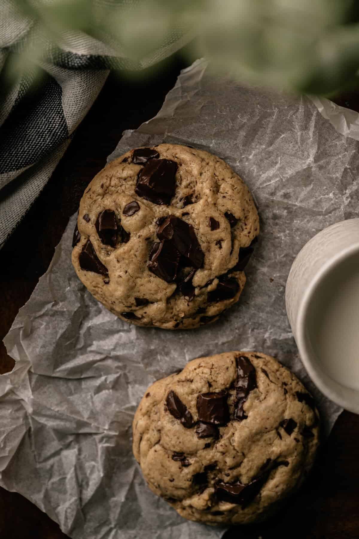  A small batch of chocolate chip cookies cooling on a table with a glass of milk