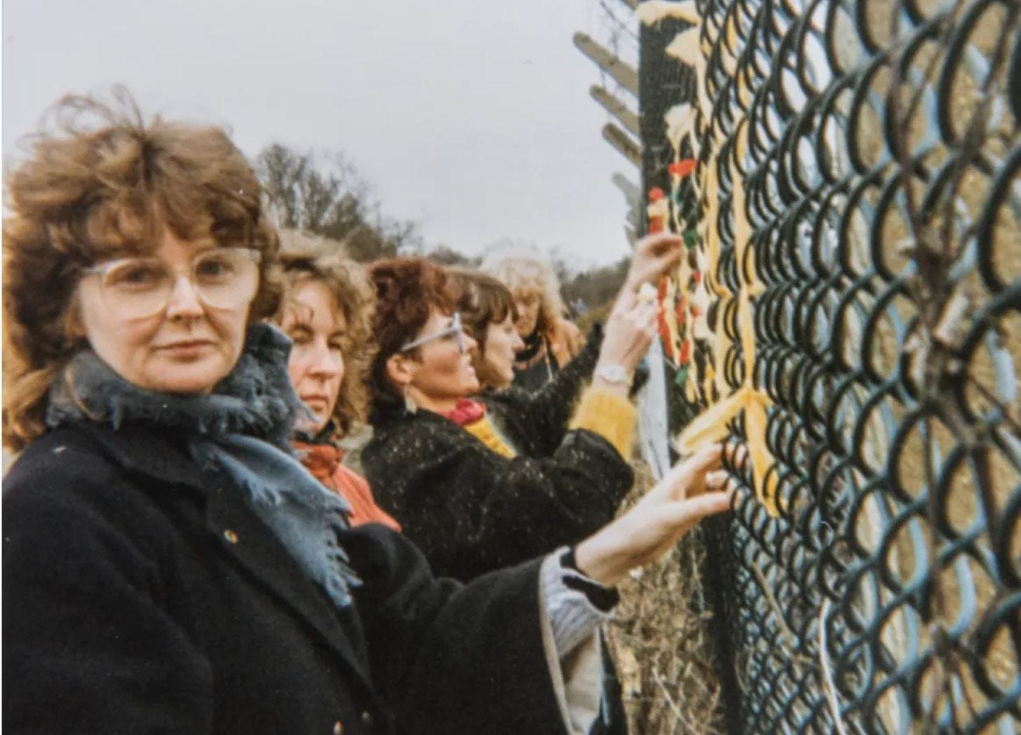 Women protesters line up facing tall wire fence. Women protesters line up facing tall wire fence.