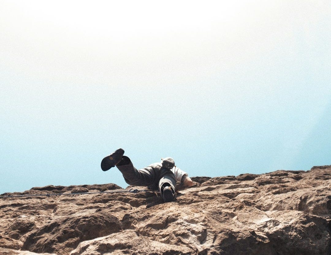 silhouette of man sitting on rock formation during daytime