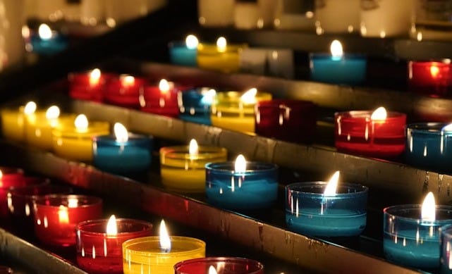 many lit candles are lined up in rows