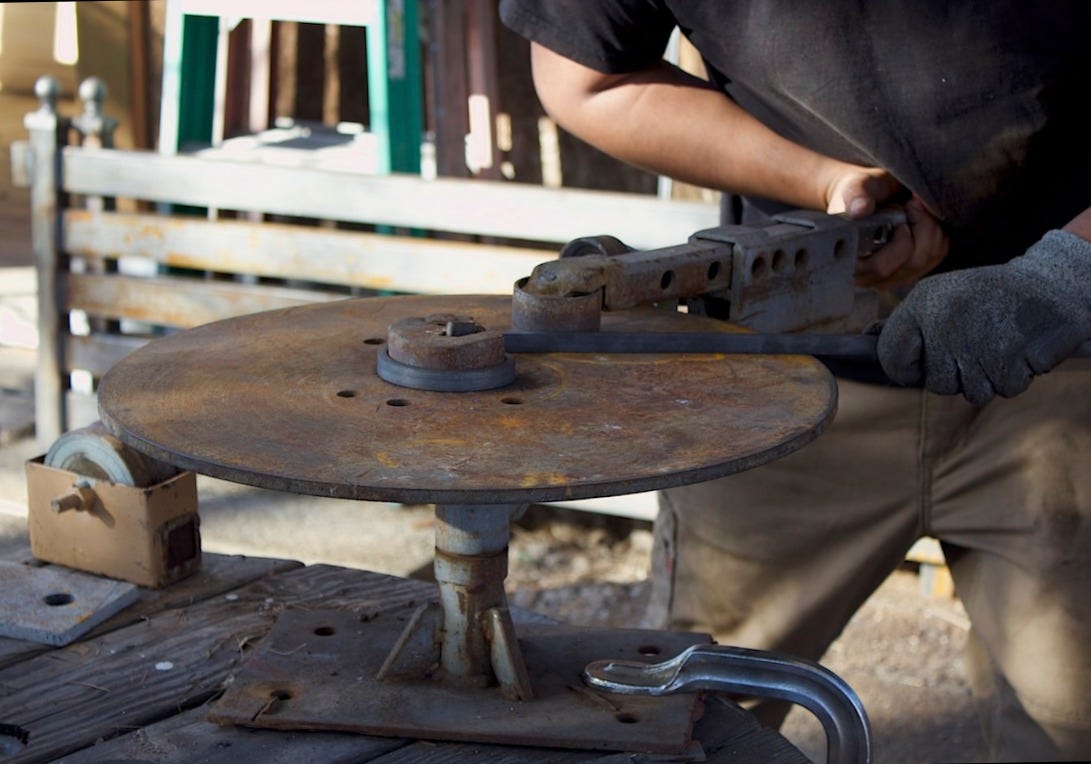 Hands operating a manual metal bender, shaping a strip of steel on a workbench.