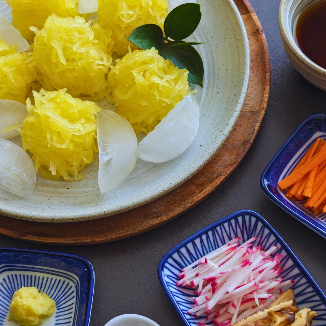 Mounds of spaghetti squash strands styled like somen noodles on a large plate surrounded by ice cubes, with colorful toppings and dipping sauce on the side