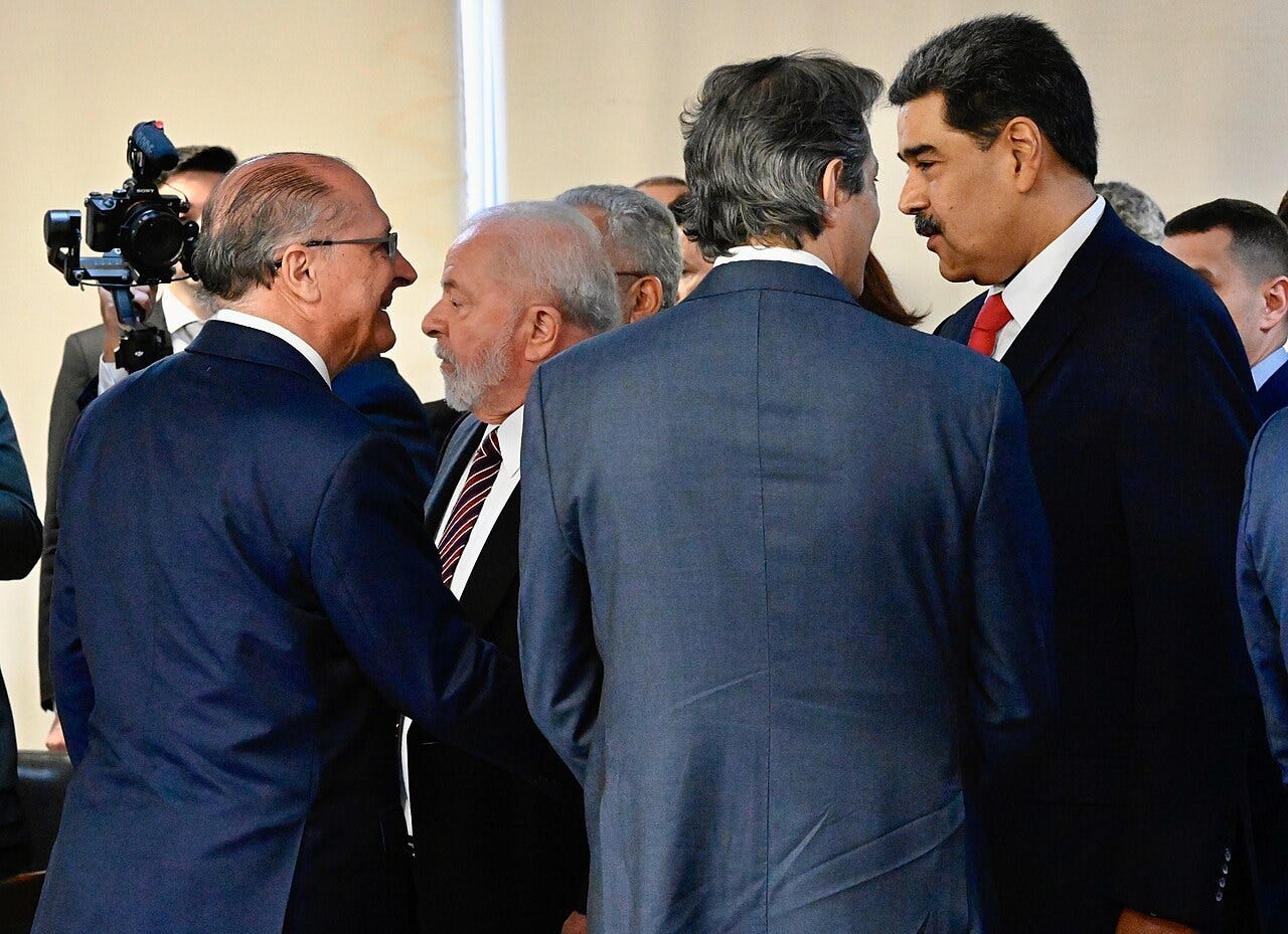 Brazilian Vice President Geraldo Alckmin and President Lula, seen from the side, talk with Venezuela's Nicolás Maduro, standing on the right in a dark suit and red tie, among officials in a room of the Planalto Palace. Brazilian Vice President Geraldo Alckmin and President Lula, seen from the side, talk with Venezuela's Nicolás Maduro, standing on the right in a dark suit and red tie, among officials in a room of the Planalto Palace.