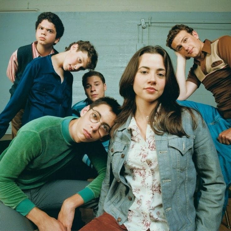 This may contain: a group of young people sitting next to each other in front of a white wall